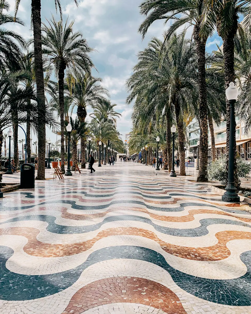 Wellenförmiges Mosaikpflaster der Explanada de España in Alicante, gesäumt von hohen Palmen und Laternen