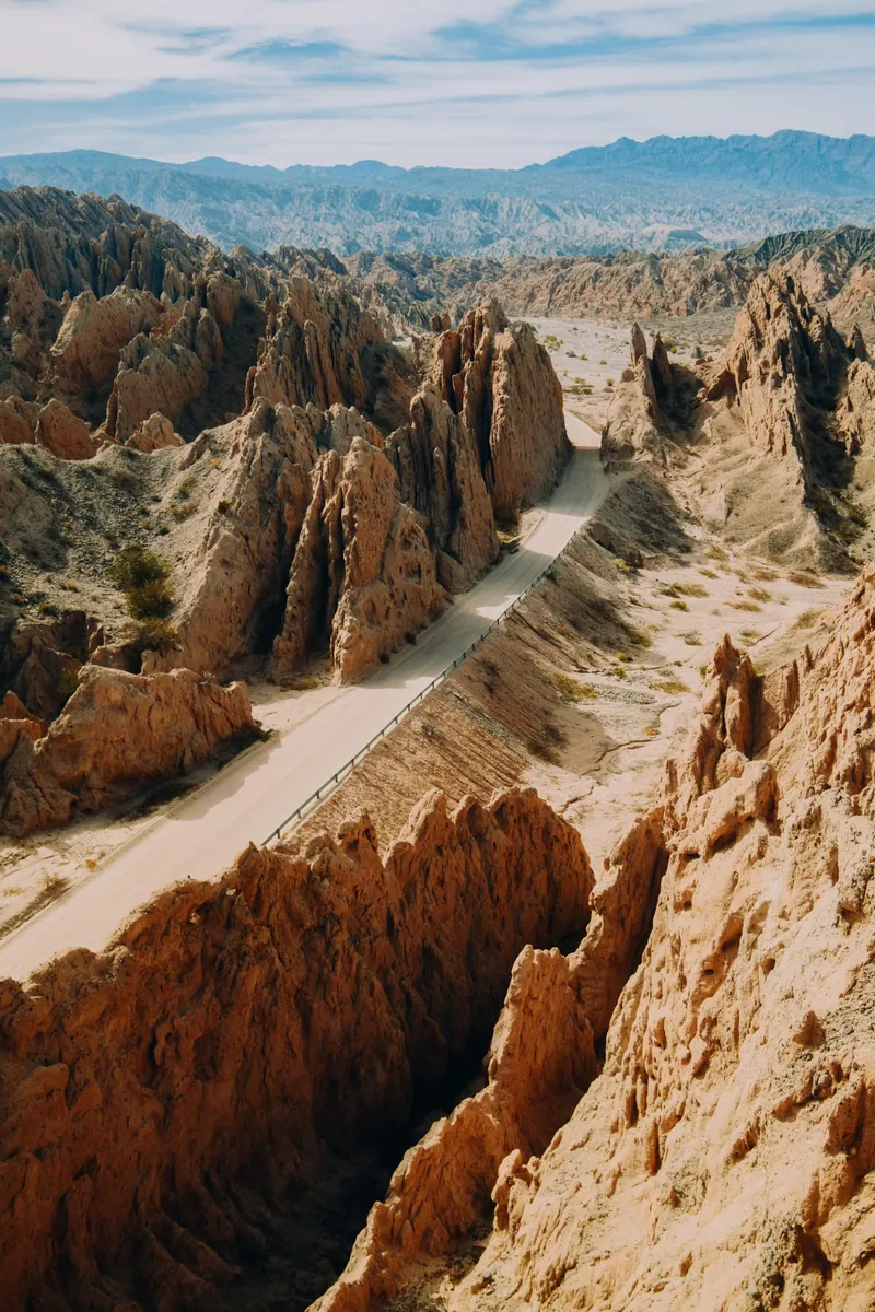 Eine Straße schlängelt sich durch eine Schlucht mit scharfkantigen, schräg aufragenden Sandsteinfelsen, dahinter Bergketten