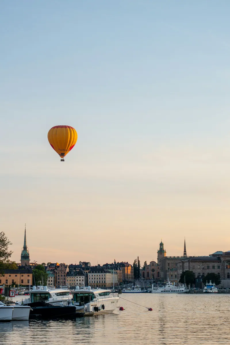 Heißluftballon über der Altstadt Gamla Stan in Stockholm, davor Motorboote am Kai im warmen Dämmerlicht