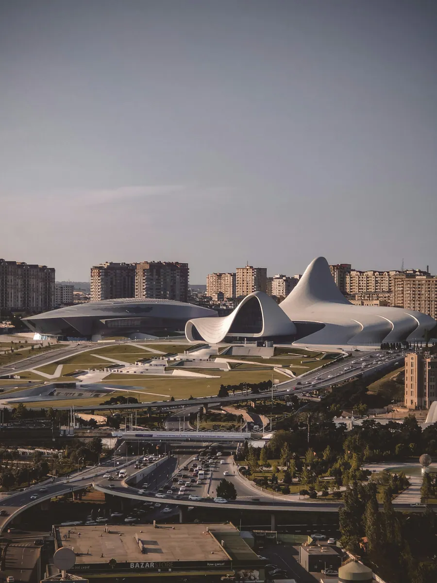 Heydar-Alijew-Zentrum in Baku mit seinen geschwungenen weißen Formen, davor Grünanlagen und eine belebte Straßenkreuzung