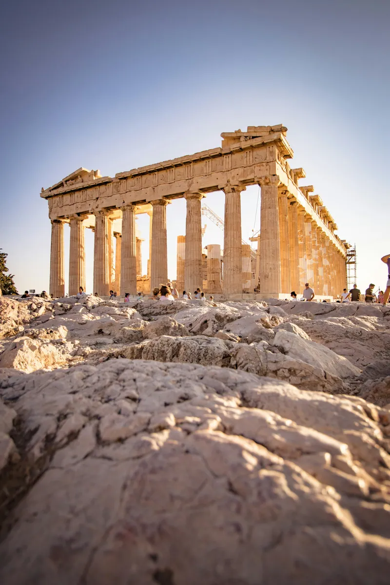 Parthenon auf der Akropolis in Athen im warmen Nachmittagslicht, im Vordergrund heller Fels und Besucher