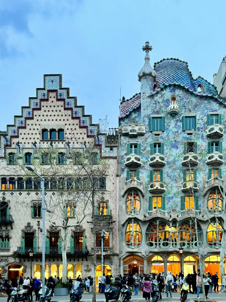 Fassaden der Casa Batlló und der Casa Amatller in Barcelona mit Mosaikschmuck, davor Passanten und Motorroller