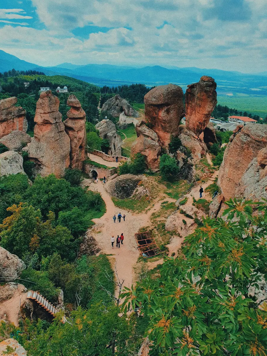 Rote Sandsteinsäulen und Felstürme mit Wanderwegen und alten Festungsmauern, im Hintergrund ein weites Tal mit Bergen