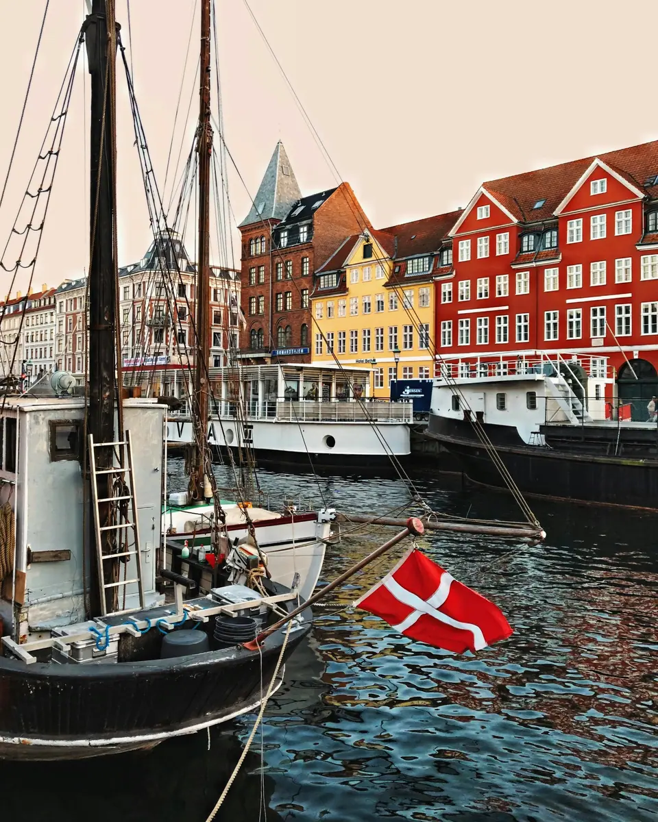 Bunte Giebelhäuser am Nyhavn in Kopenhagen, im Vordergrund ein Segelschiff mit dänischer Flagge
