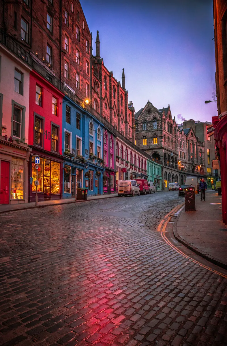 Geschwungene Victoria Street in Edinburgh mit farbigen Ladenfronten und Kopfsteinpflaster in der Abenddämmerung
