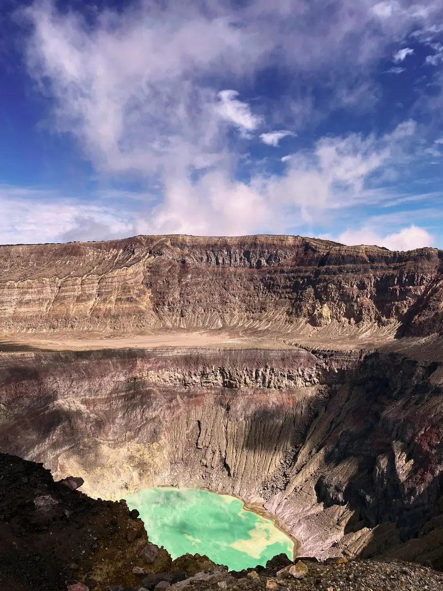 Blick in einen Vulkankrater mit geschichteten Wänden und einem türkisgrünen Kratersee am Grund