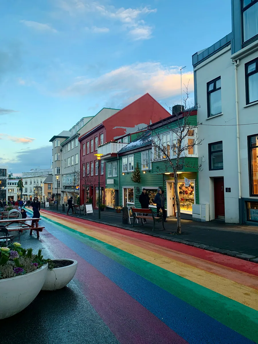 In Regenbogenfarben bemalte Straße mit bunten Häusern, beleuchteten Schaufenstern und Weihnachtsschmuck