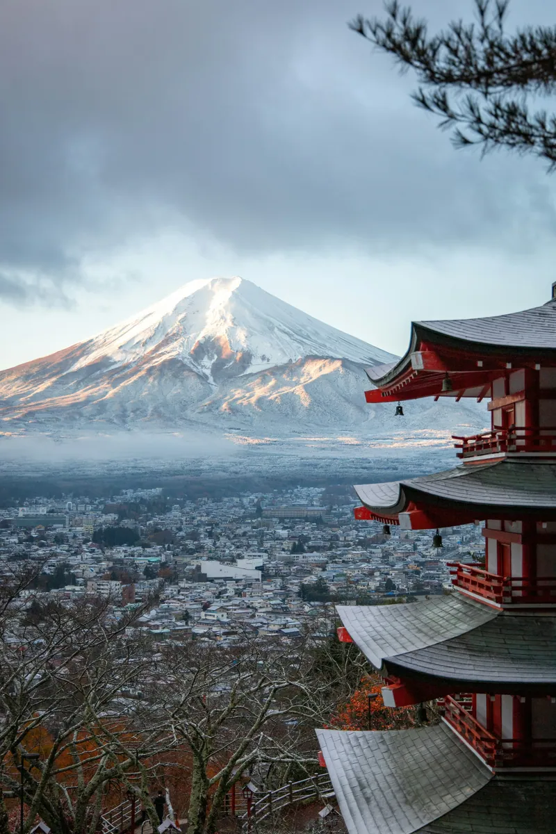 Schneebedeckter Fuji über einer Stadt im Tal, rechts im Vordergrund die rote Chureito-Pagode