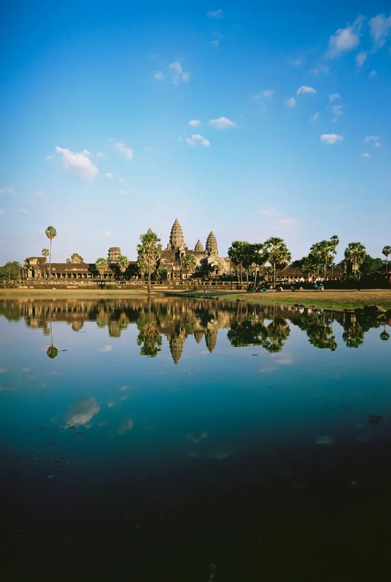 Die Türme von Angkor Wat und Palmen spiegeln sich in einem ruhigen Teich unter blauem Himmel