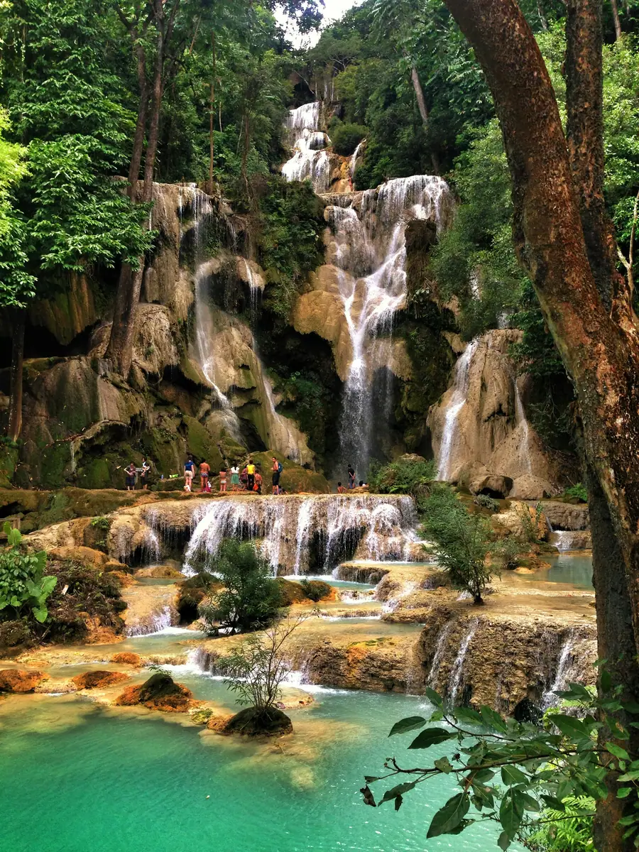 Wasserfall stürzt über Kalksteinterrassen in türkisfarbene Becken im Dschungel, oben stehen Besucher