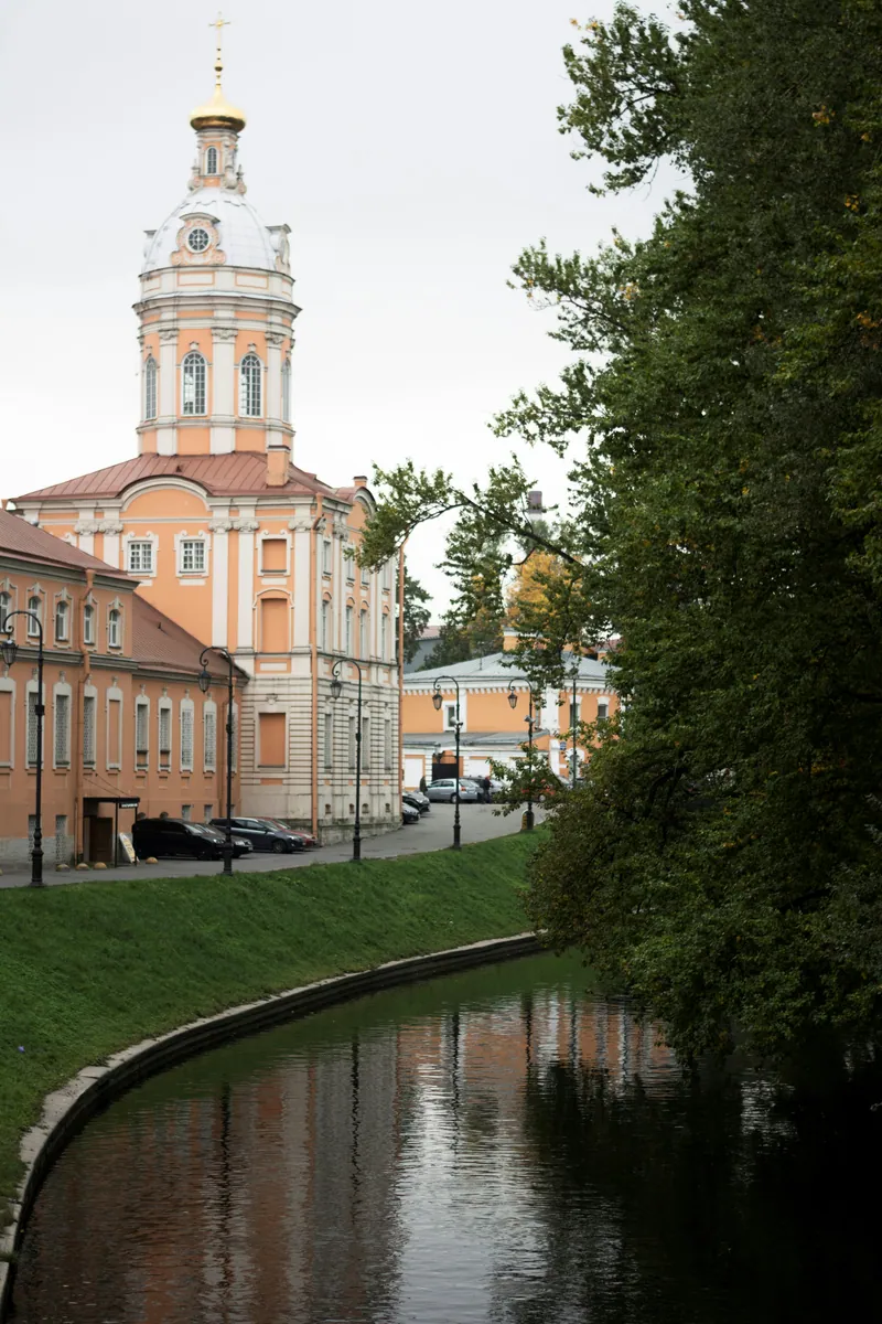 Barockes Gebäude mit Kuppelturm und goldenem Kreuz an einem schmalen Kanal mit grüner Uferböschung