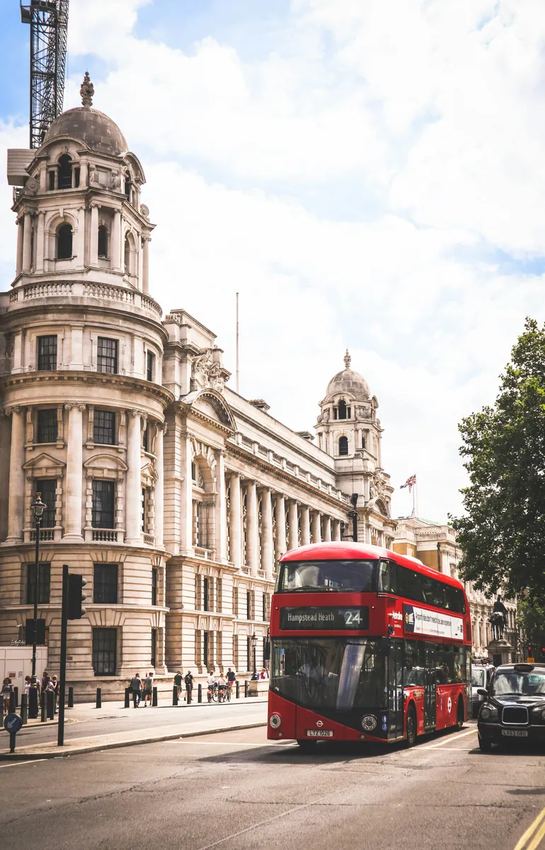 Roter Doppeldeckerbus und schwarzes Taxi vor einem prunkvollen Kuppelbau mit Säulen in London