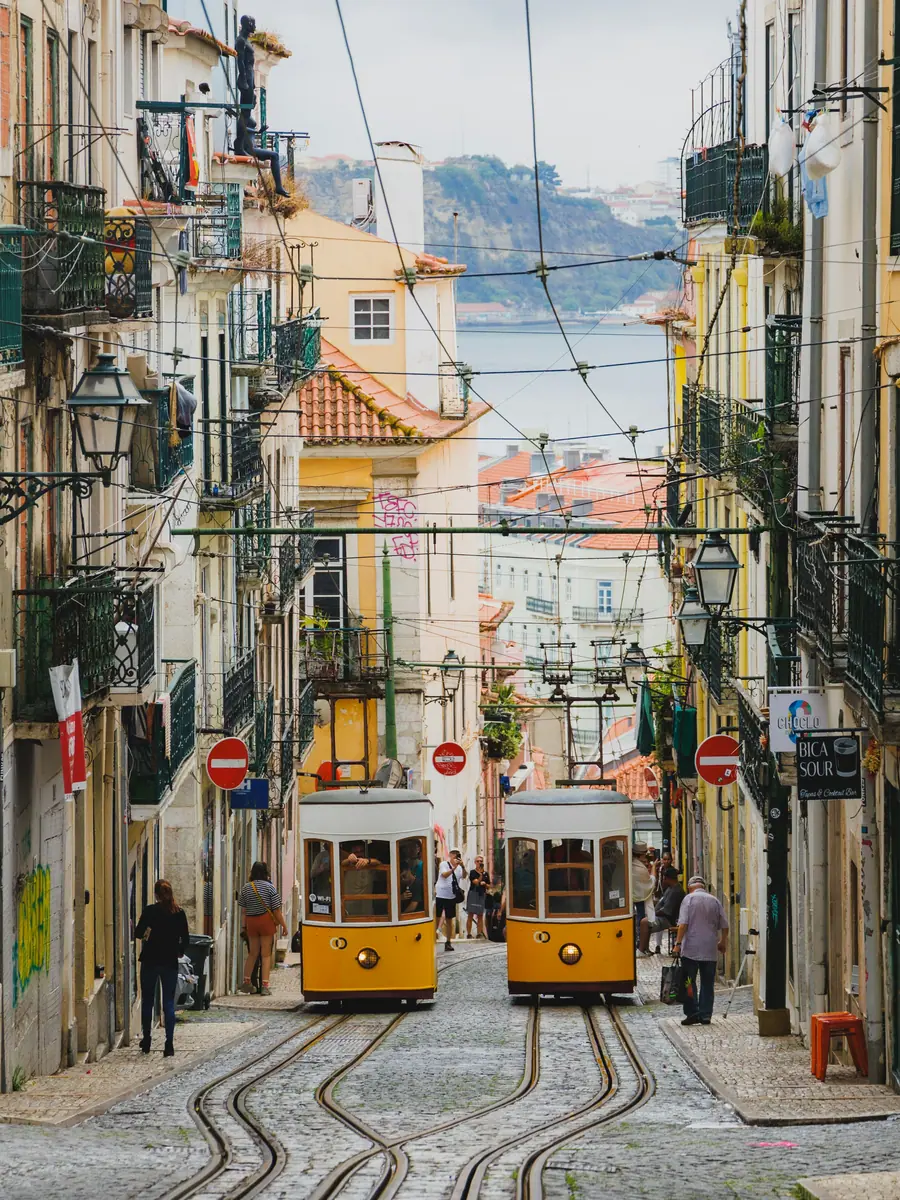 Zwei gelbe Wagen der Standseilbahn Ascensor da Bica in einer steilen Gasse in Lissabon, hinten der Tejo