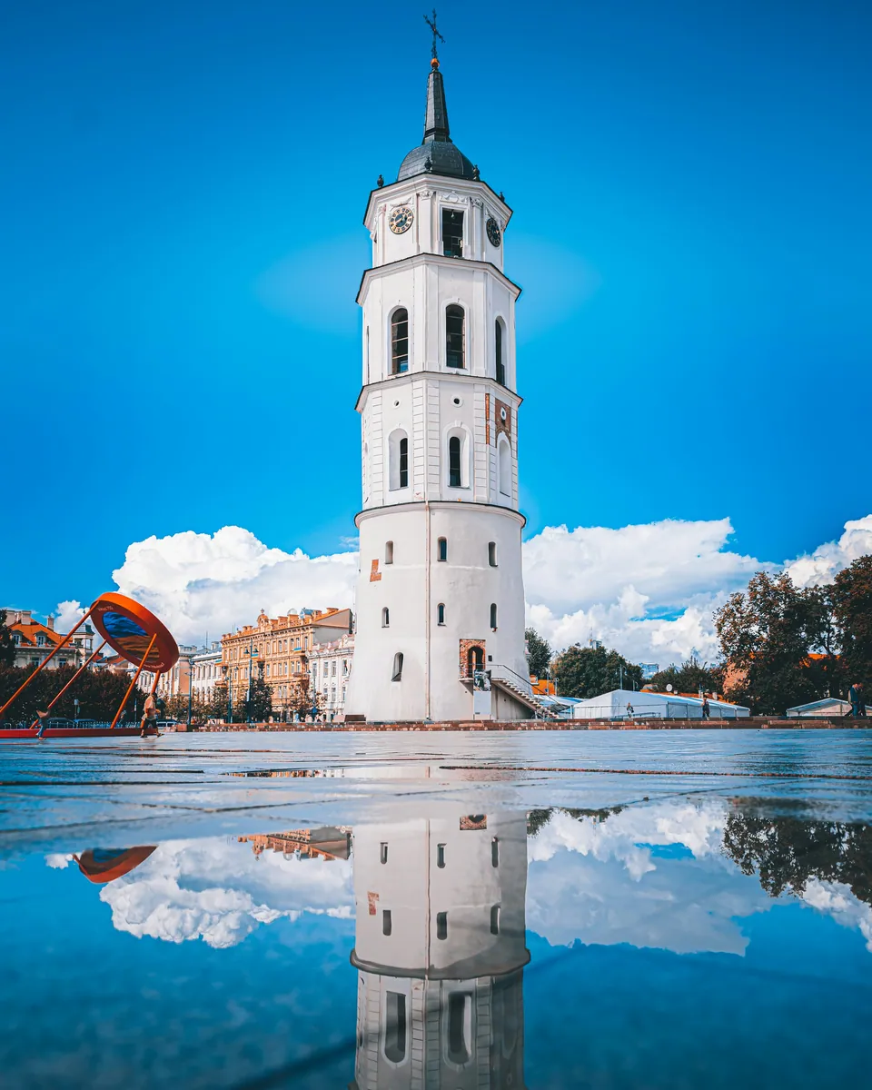 Weißer Glockenturm der Kathedrale von Vilnius, der sich in einer Pfütze auf dem Kathedralenplatz spiegelt