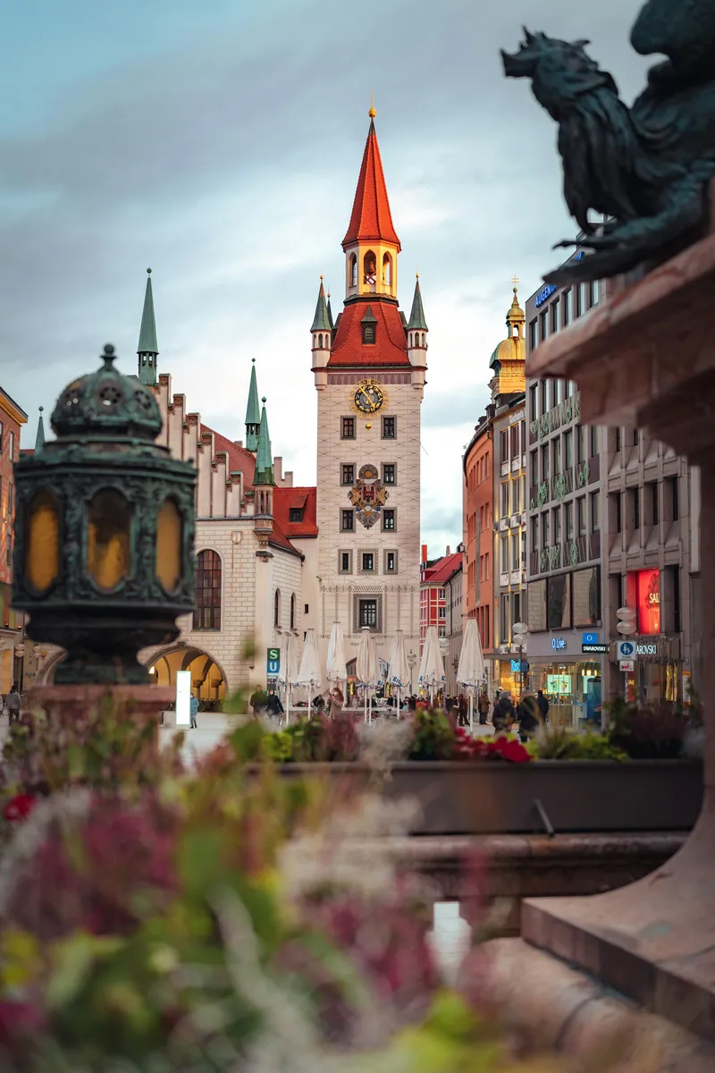 Altes Rathaus am Marienplatz in München mit rotem Turmhelm, im Vordergrund eine Bronzefigur und Blumen