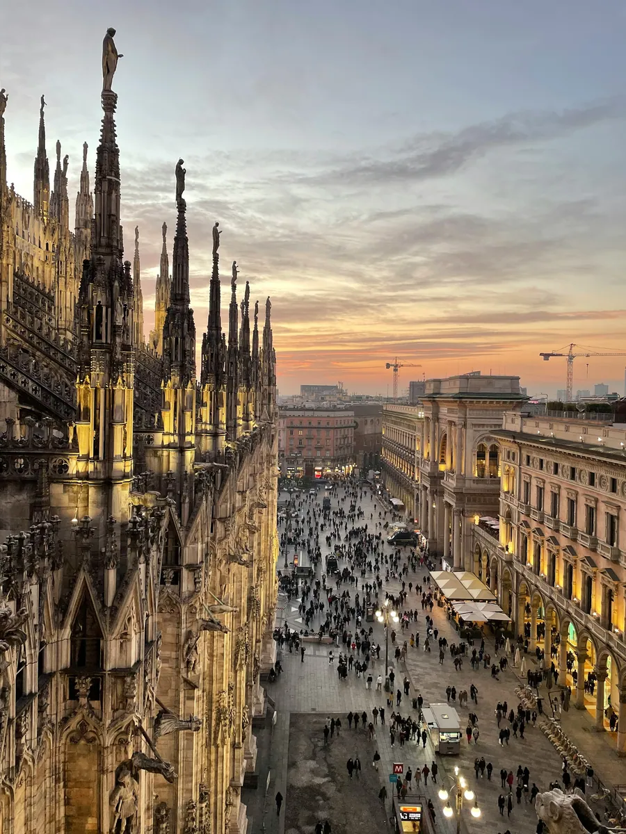 Gotische Turmspitzen des Mailänder Doms mit Blick auf den belebten Domplatz bei Sonnenuntergang
