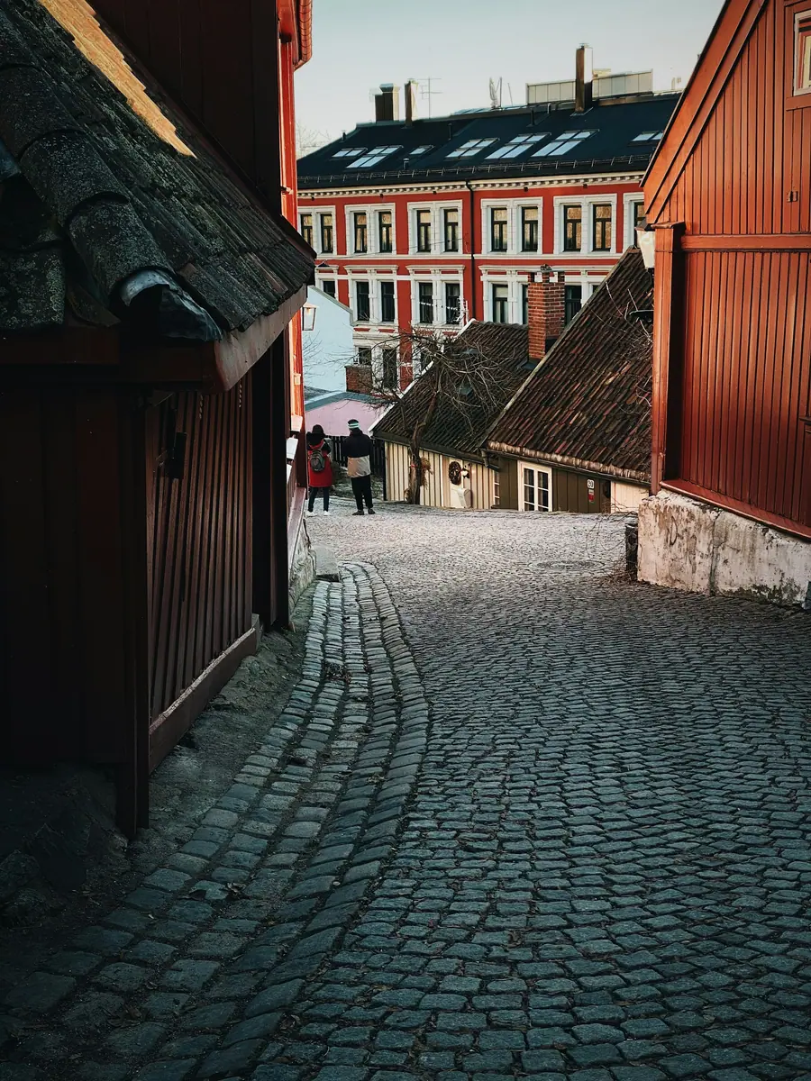 Kopfsteinpflastergasse zwischen alten roten Holzhäusern, im Hintergrund ein Stadthaus mit roter Fassade