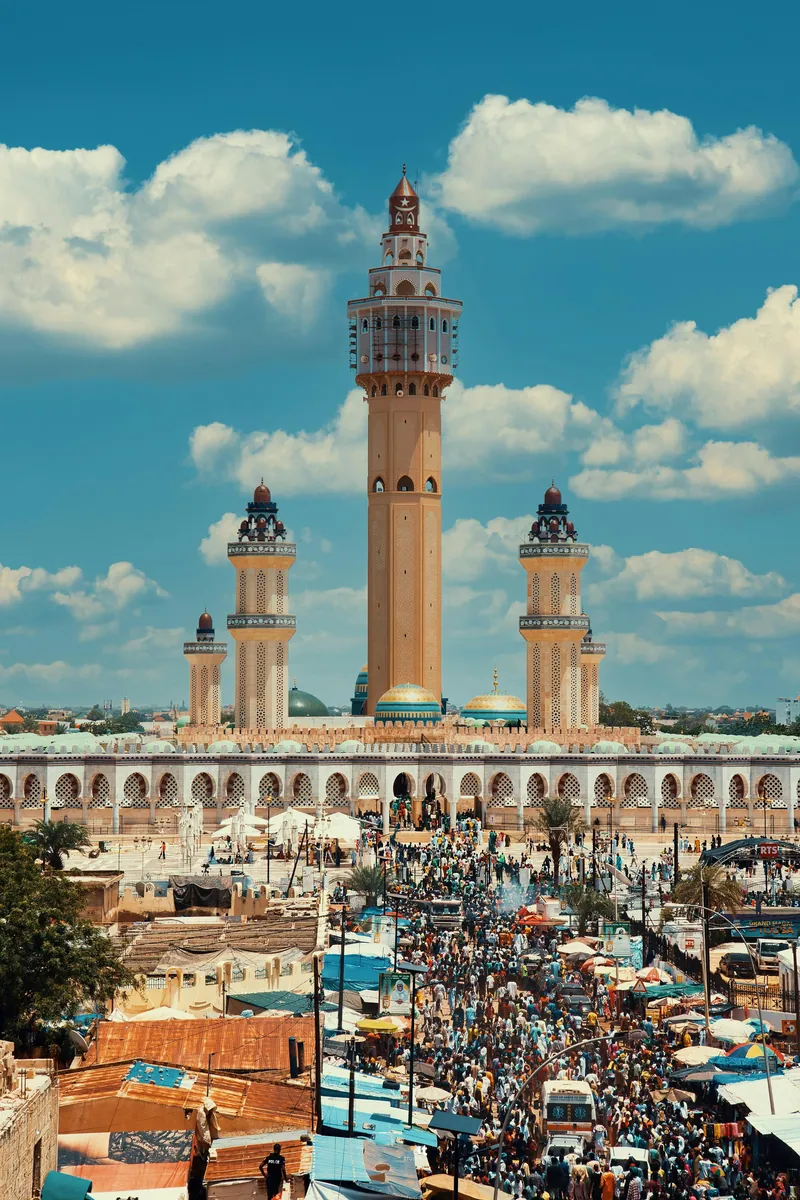 Große Moschee mit hohem Mittelminarett und mehreren Seitenminaretten, davor eine dicht gedrängte Menschenmenge.