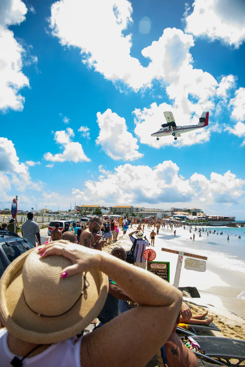 Ein Propellerflugzeug fliegt im Landeanflug tief über den Maho Beach, wo Zuschauer dicht gedrängt am Strand stehen.