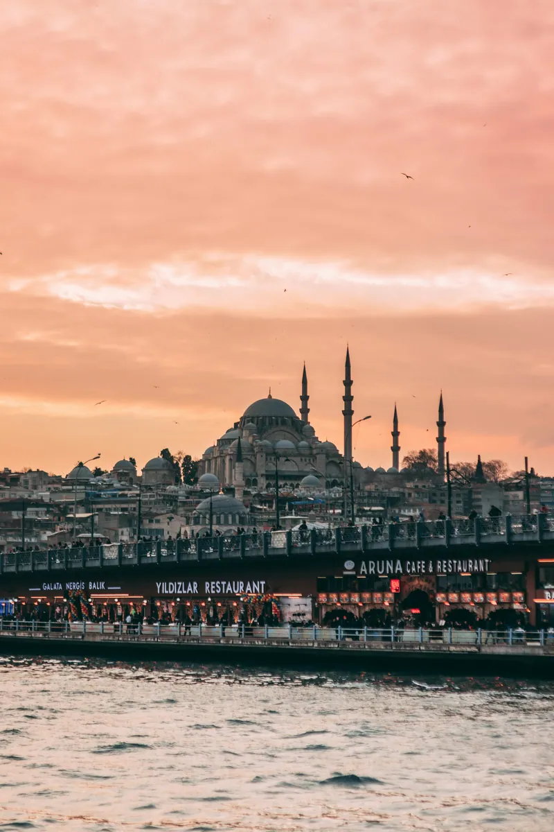 Süleymaniye-Moschee in Istanbul über der Galatabrücke mit Restaurants am Wasser bei rosa Abendhimmel