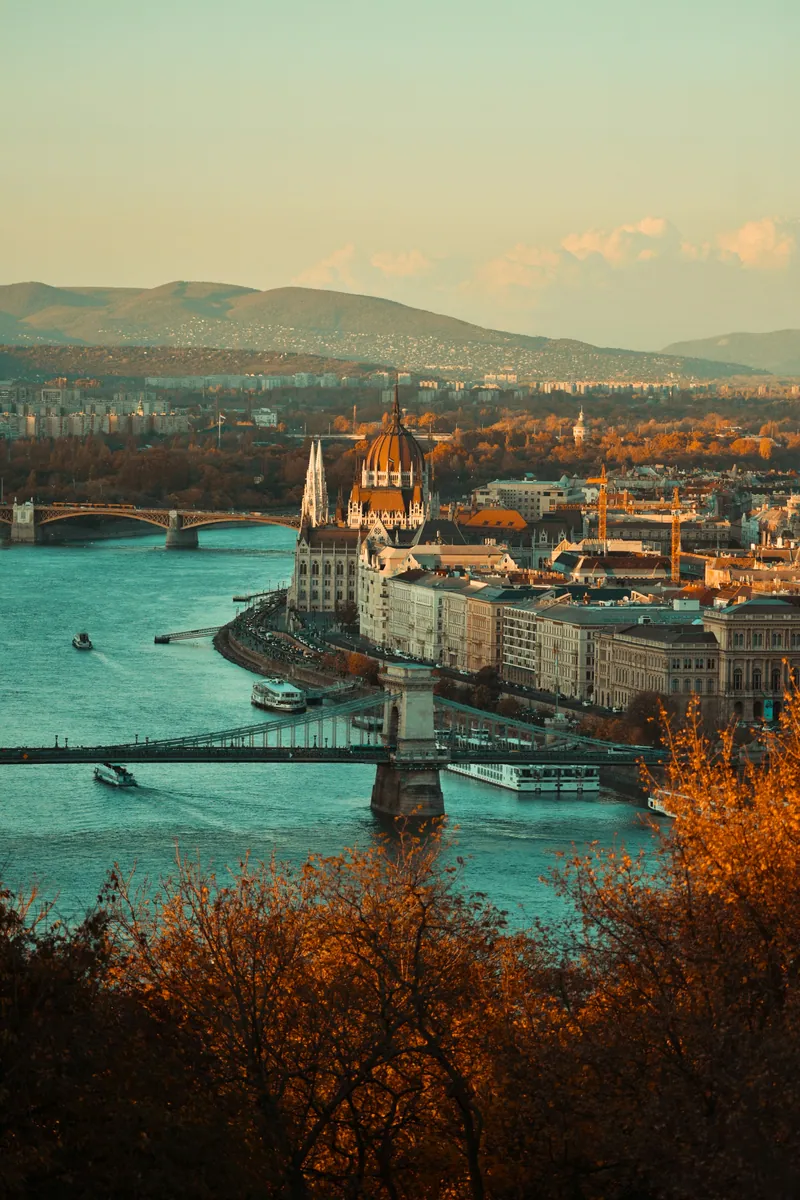 Blick über die Donau in Budapest auf das Parlamentsgebäude und die Kettenbrücke, im Vordergrund Herbstlaub