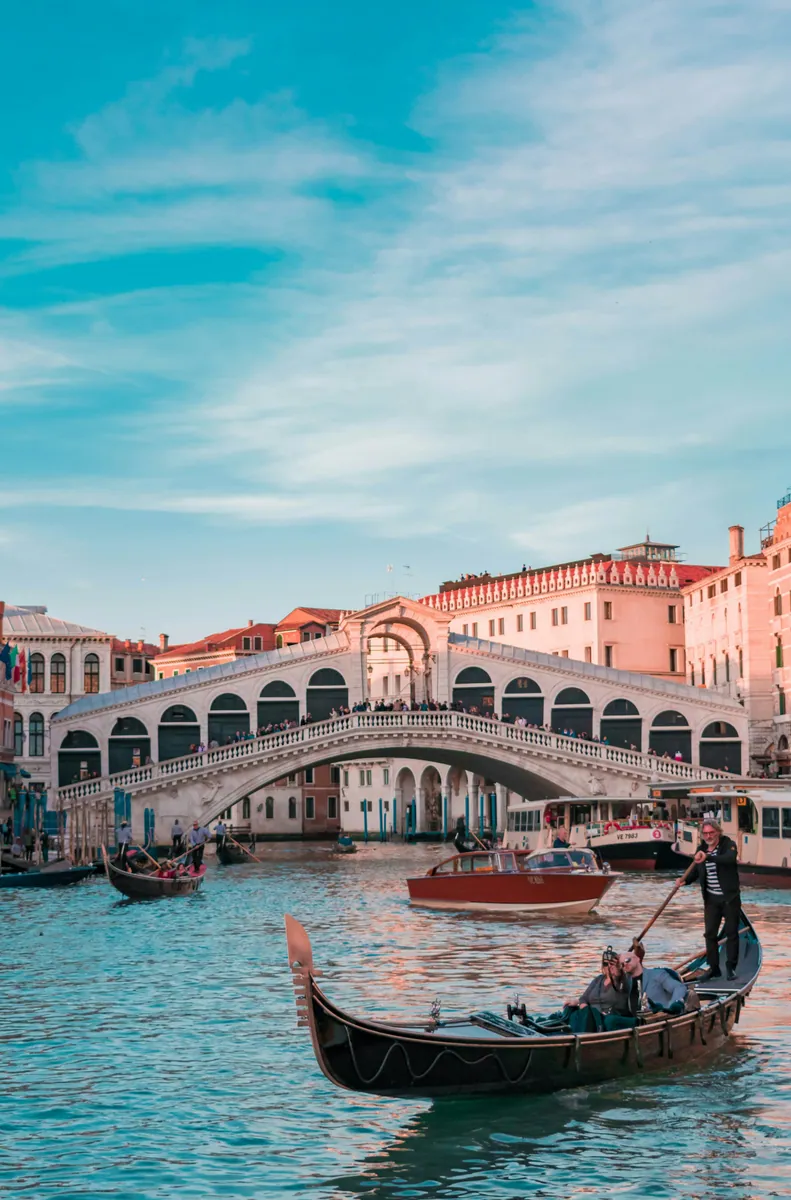 Rialtobrücke über den Canal Grande in Venedig, davor eine Gondel mit Fahrgästen und ein hölzernes Motorboot