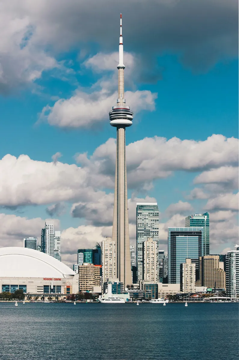 CN Tower über der Skyline von Toronto am Ontariosee, links das Kuppeldach des Rogers Centre, darüber Quellwolken